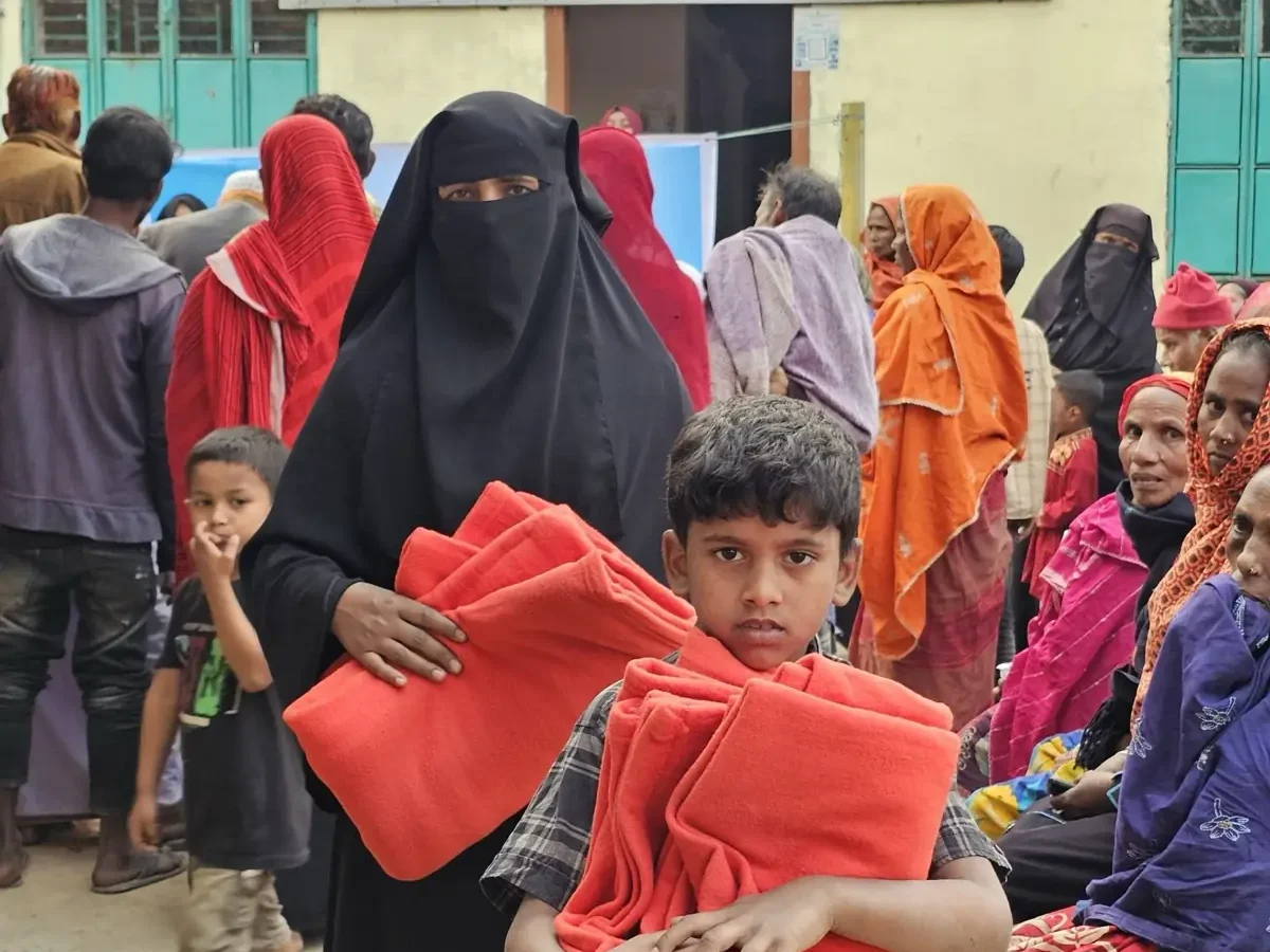 A boy carries two folded blankets away from the distribution point as families queue behind him, January 2025