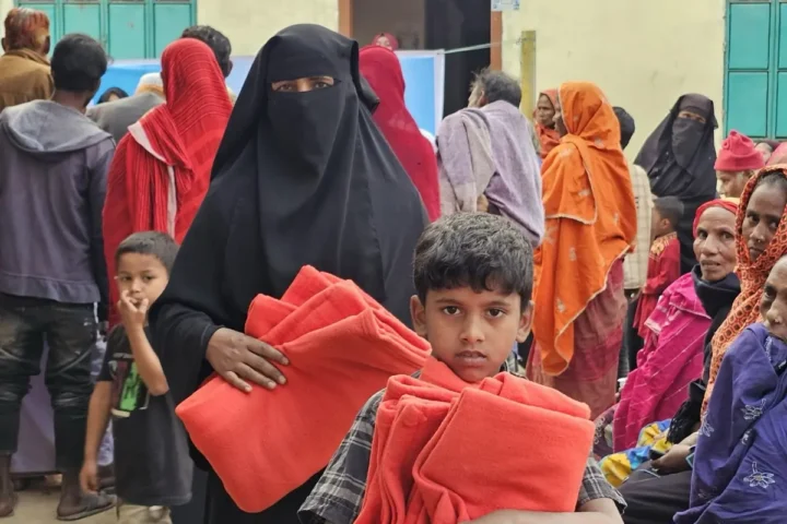 A boy carries two folded blankets away from the distribution point as families queue behind him, January 2025