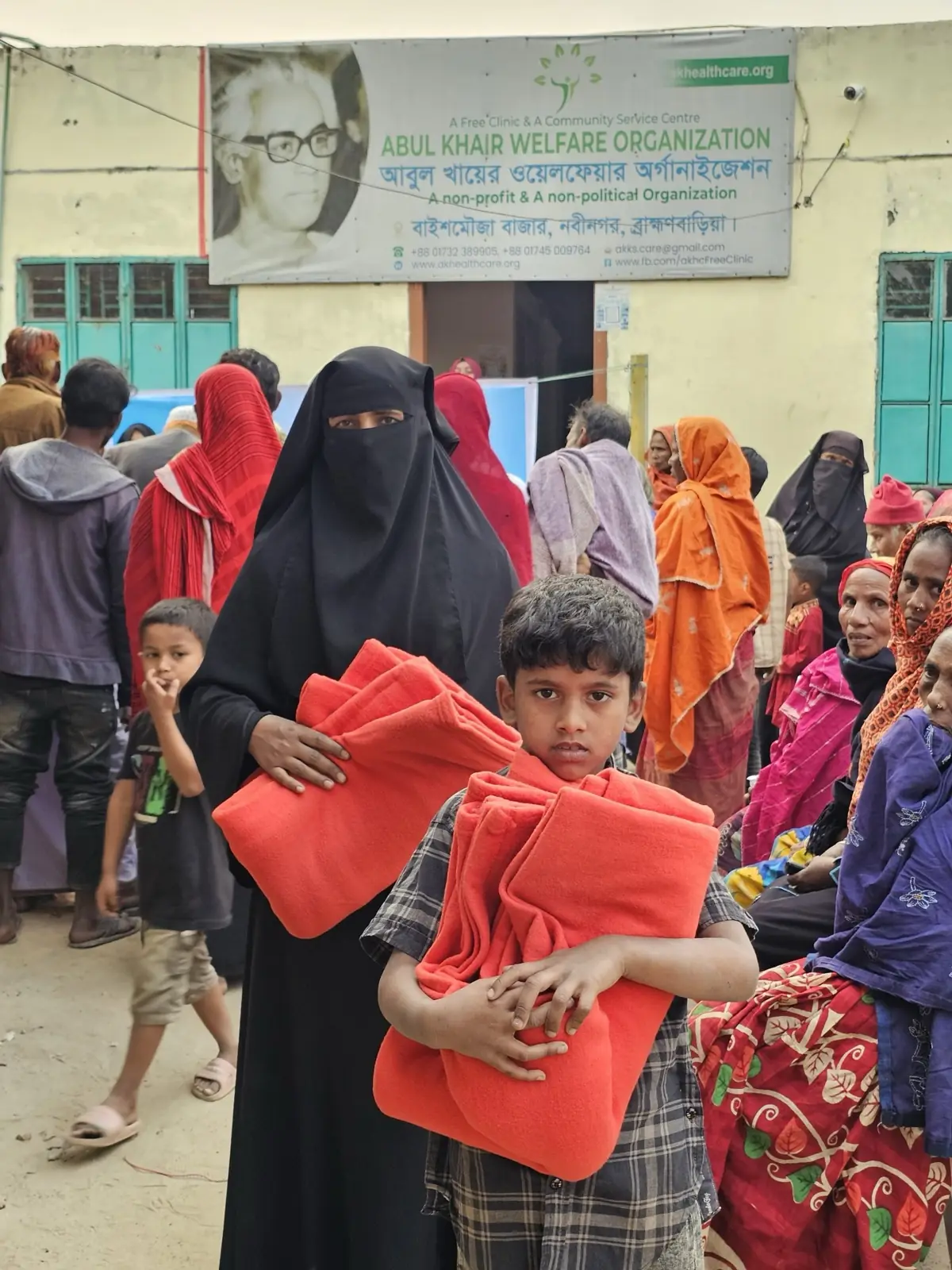 A boy carries two folded blankets away from the distribution point as families queue behind him, January 2025