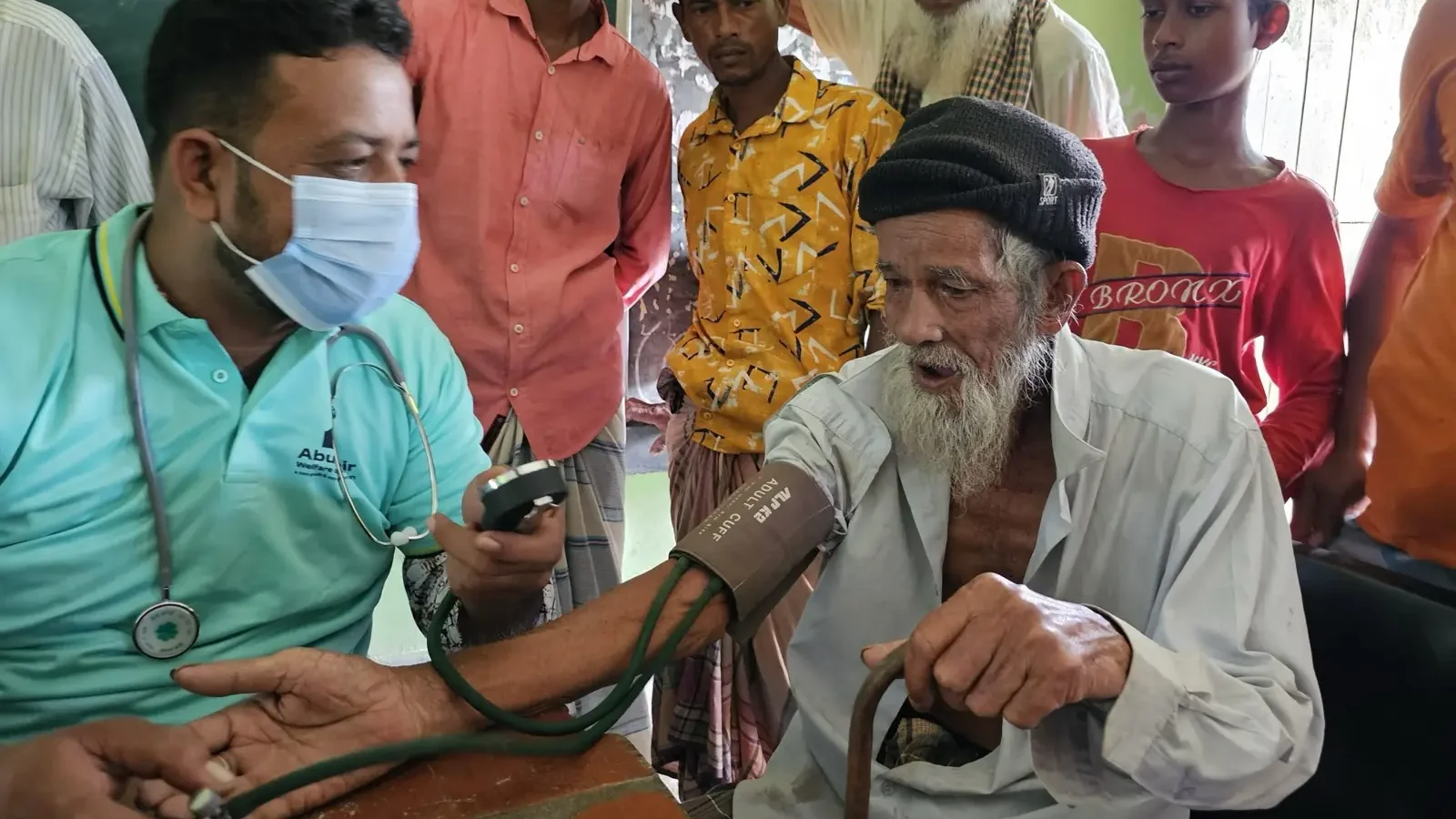 A health worker checks an elderly man's blood pressure while other patients wait their turn at the free Friday clinic in Baishmouja, September 2024