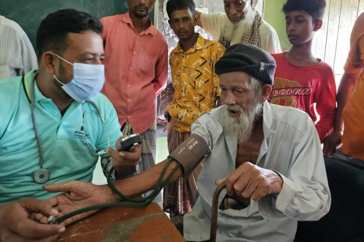 A health worker checks an elderly man's blood pressure while other patients wait their turn at the free Friday clinic in Baishmouja, September 2024