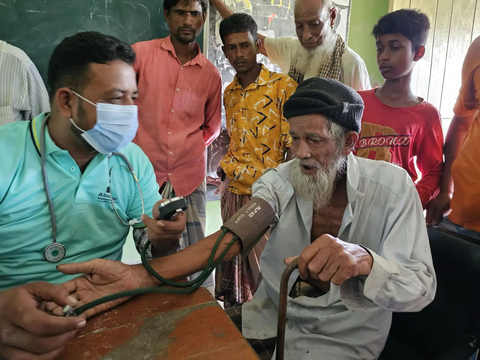 A health worker checks an elderly man's blood pressure while other patients wait their turn at the free Friday clinic in Baishmouja