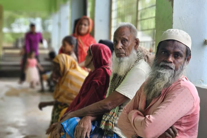 Two elderly men wait on a bench among other patients at the free Friday clinic in Baishmouja
