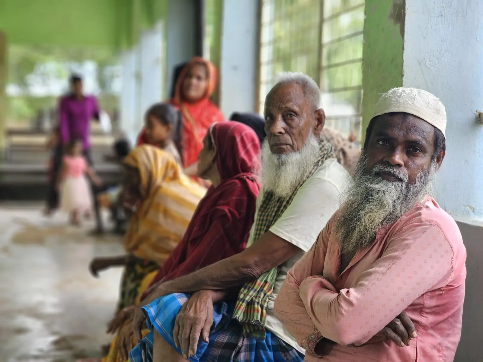 Two elderly men wait on a bench among other patients at the free Friday clinic in Baishmouja