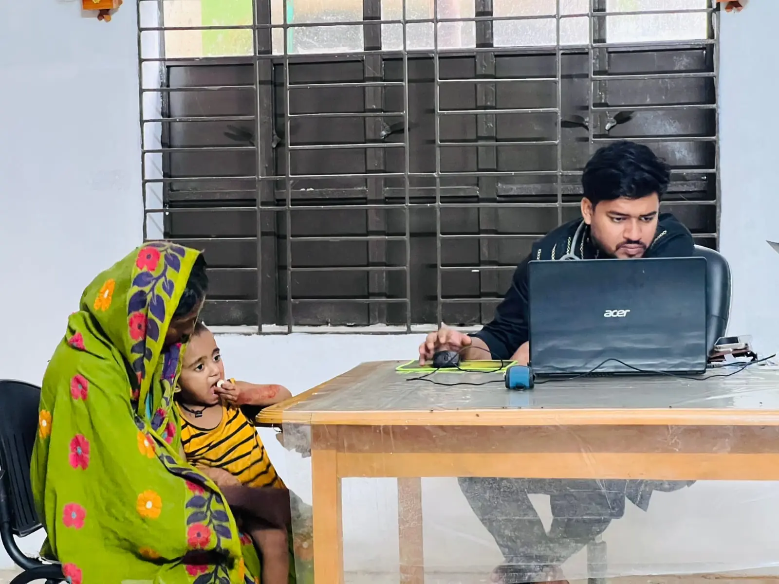 A mother and her child sit with an AKWO worker registering patients at the free medical camp on 1 May 2026