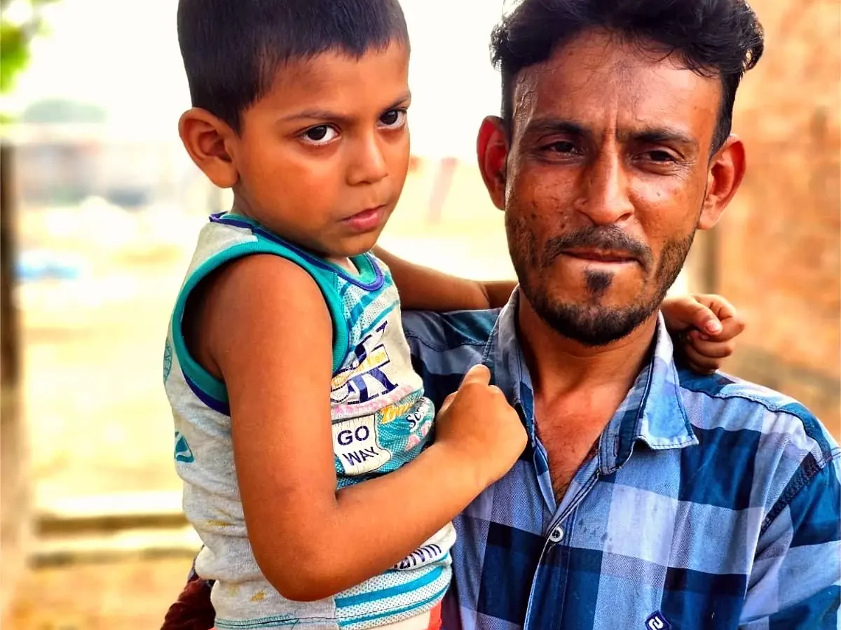 Masud holds his son outside their home in Nabinagar