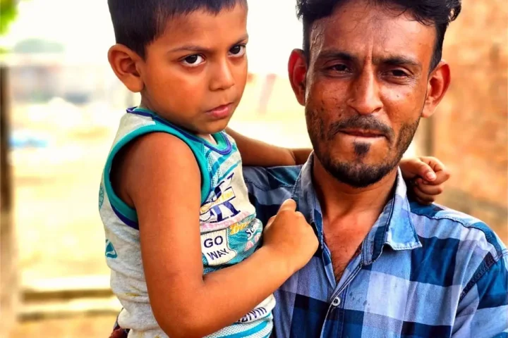 Masud holds his son outside their home in Nabinagar