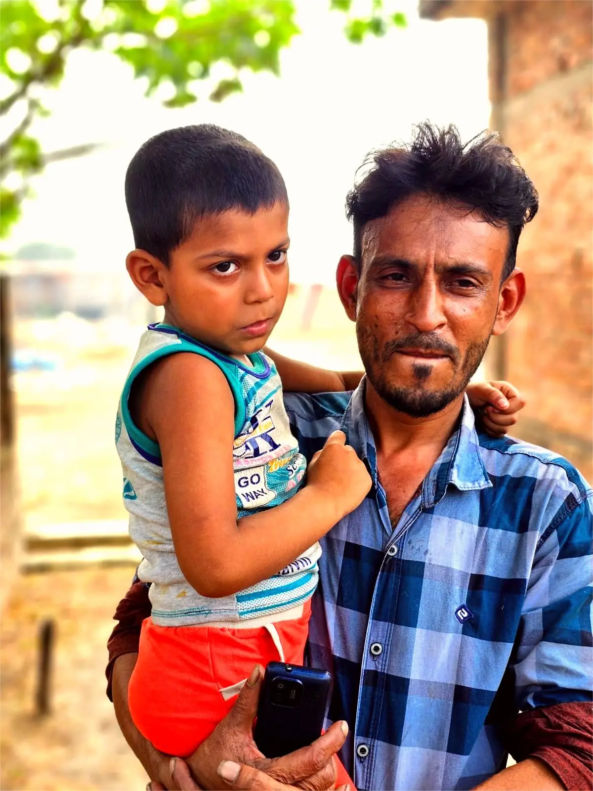 Masud holds his son outside their home in Nabinagar