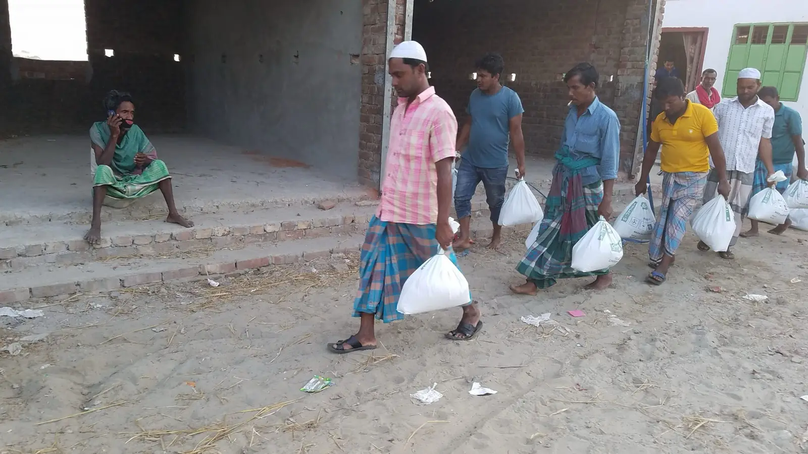 AKWO-র বিতরণ কেন্দ্র থেকে খাদ্য ত্রাণের প্যাকেট নিয়ে যাচ্ছেন পুরুষেরা
