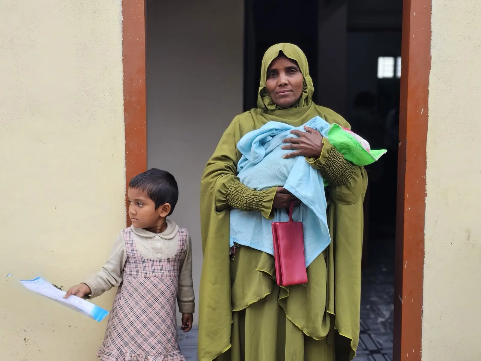 A mother carries the blanket and supplies she has just received while her daughter holds a leaflet, January 2025