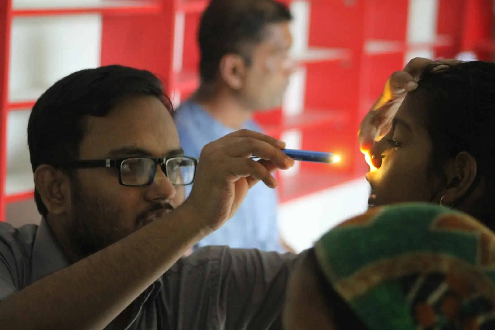 A doctor examines a patient's mouth with a torch at a village health camp in 2019